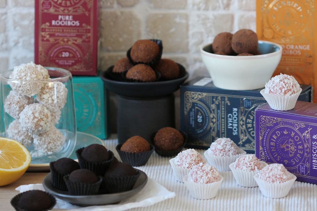 Selection of five types of chocolate truffles, each made with a different flavoured tea, beautifully displayed on a selection of tiny plates and crockery in front of the tea products that were used to make the truffles.
