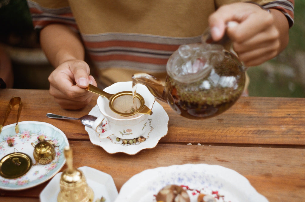 Person pouring Wild Grown Rooibos into a strainer/infuser that is over a teacup