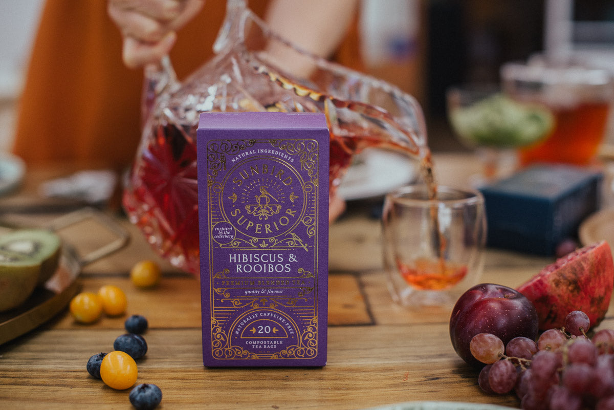 Hibiscus and rooibos tea box by Sunbird Rooibos, in front of a fresh pot of healthy rooibos being poured into a tea cup